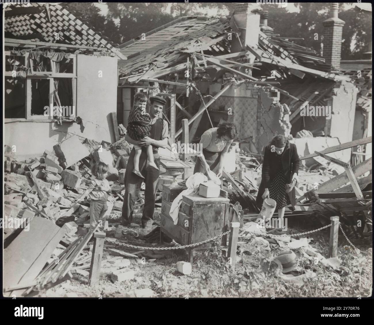 BOMBE ZERSTÖRTE DEN BUNGALOW, ABER DIE FAMILIE WAR SICHER IM UNTERSCHLUPF. Obwohl der Bungalow der Familie Griggs im Südosten Englands durch eine deutsche Bombe zerstört wurde, war die Familie, einschließlich zweier kleiner Kinder, in ihrem Anderson-Schutzhaus sicher. Die Raider, die versuchten, Londons Verteidigung zu durchdringen, stießen auf eine enorme Flugabwehrfeuer und mindestens sechs von ihnen sollen abgeschossen worden sein. FOTOSHOWS: Mr. Und Mrs. W. Griggs, Mrs. J. Griggs, eine Schwägerin, Morris Griggs, drei Jahre alt, und Janet Griggs, zwei Jahre alt, inmitten des Trümmers des Bungalows. 5. September 1940 ZENSUR Nr. 65366 Stockfoto