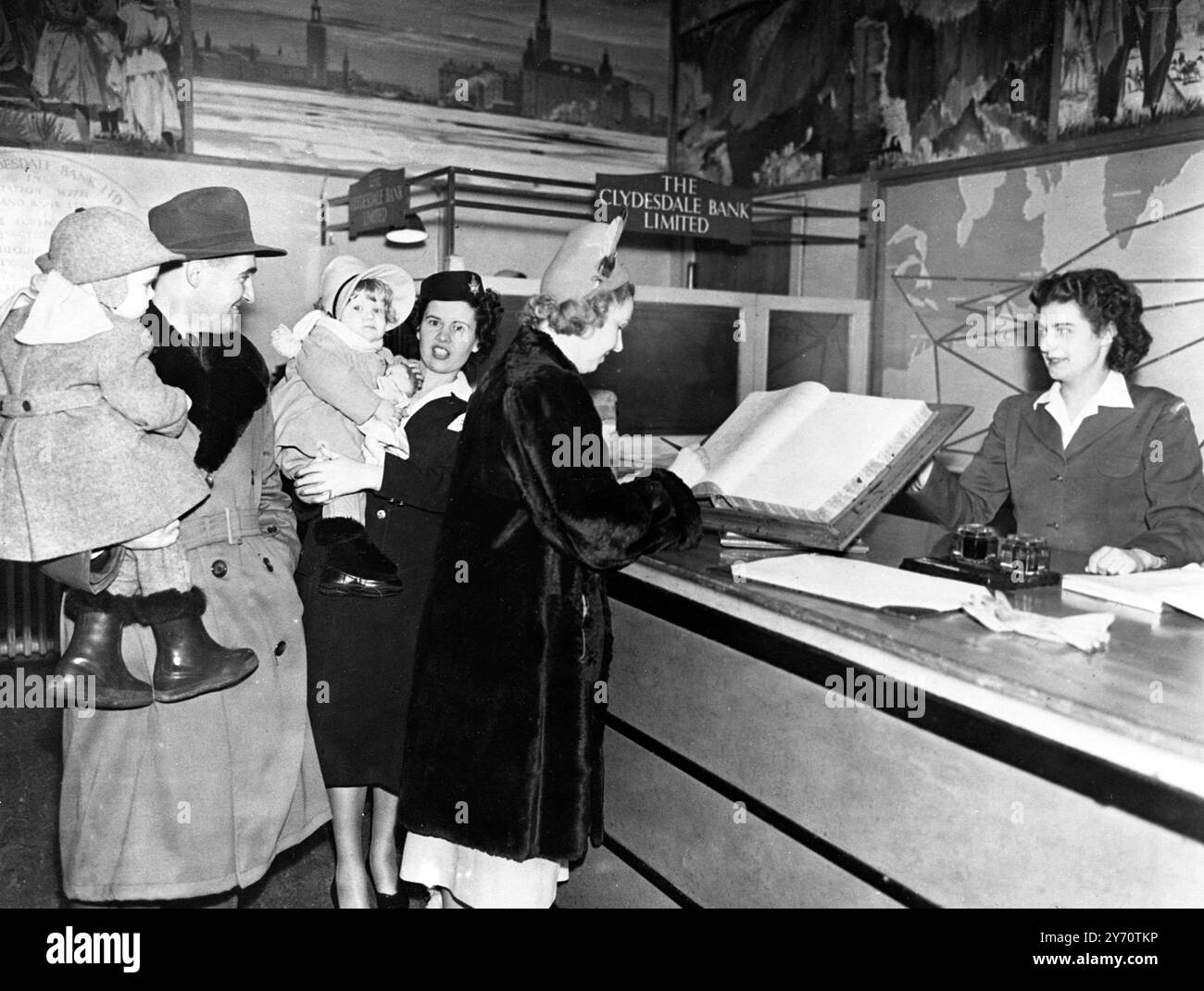 Der Flughafen Prestwick , das Zentrum eines schottischen Inlandsstreits , ist Tag und Nacht ein Hort von Aktivität . Über sein Landefeld brüllen bei jedem Wetter die Flugzeuge von einem halben Dutzend internationalen Fluggesellschaften . Britisch Kanadier , Amerikaner , Niederländer , Franzosen und Skandinavier . Eine transatlantische Familie meldet sich im Flughafenhotel Prestwick an. Frau St-Onge , eine schottische Kriegsbraut , ist aus Montreal , Kanada zurückgekehrt , um ihre Eltern nach Edinburgh zu besuchen . Mr. Ray St-Onge hält Sohn George, während Stewardess Mary O'Neill sich um die zweijährige Carol kümmert, .18. Janaury 1950 Stockfoto