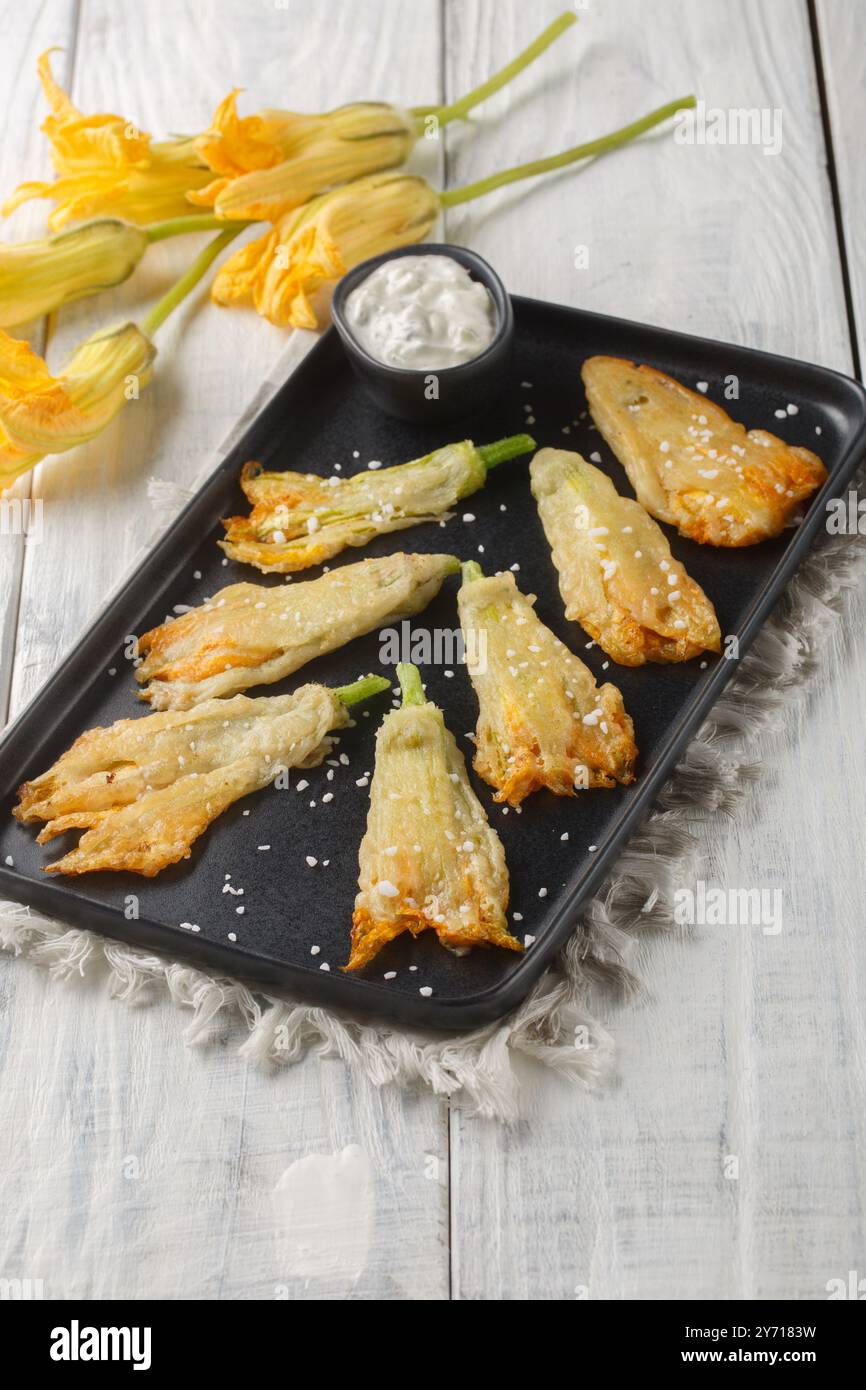 Köstliche frittierte panierte Zucchini-Blüten gefüllt mit Ricotta-Käse in Nahaufnahme auf einem Teller auf dem Tisch. Vertikal Stockfoto