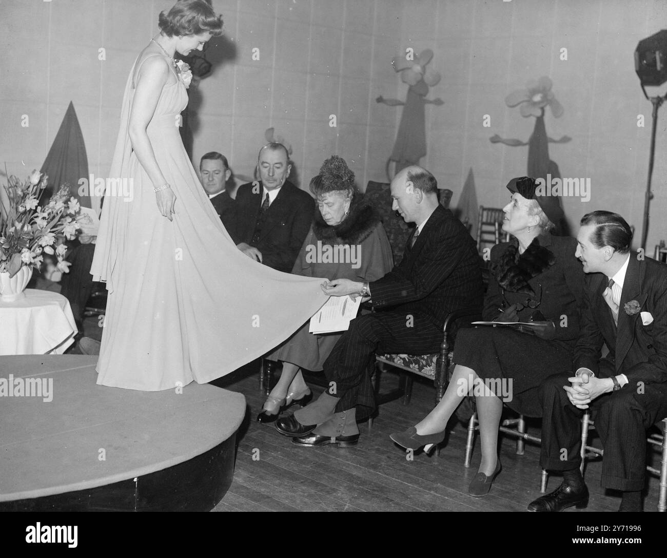 QUEEN MARY besuchte BEI DER MODESCHAU das International Wool Sekretariat , um sich ihre neueste Modeschau " Wool for Everywoman " anzusehen , eine Ausstellung von Modellen aus feinsten leichten Wollmaterialien . DAS BILD ZEIGT :- KÖNIGIN MARY inspiziert eine der Moden . Ein graues Abendkleid aus superleichter Wolle . 11. März 1949 Stockfoto