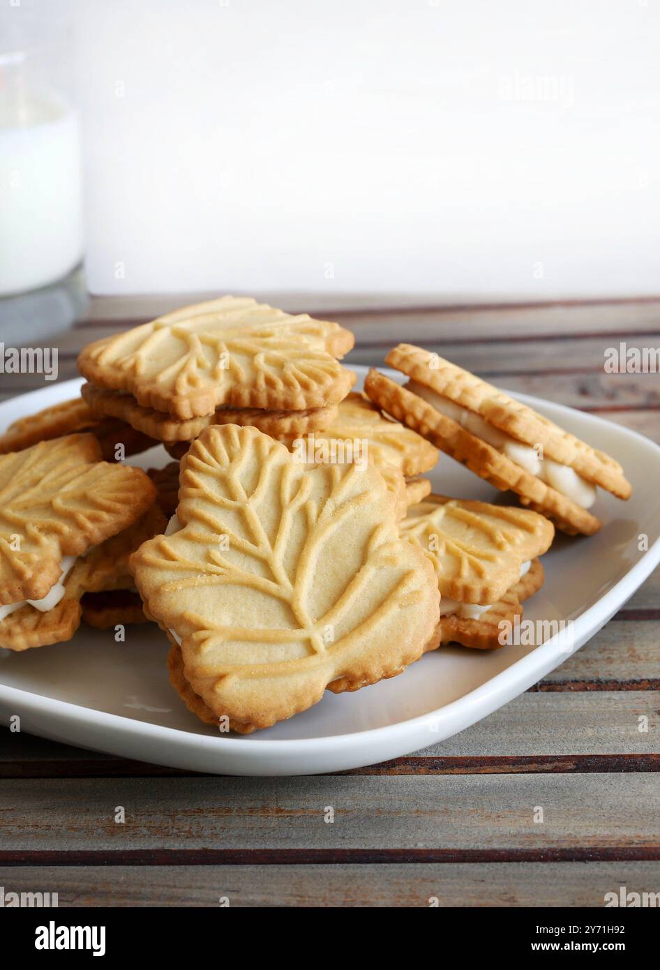 Klassische Kekse in Form eines kanadischen Ahornblatts und eine Milchgasse. Ahorncreme zwischen zwei knusprigen Keksen auf weißem Hintergrund. Stockfoto