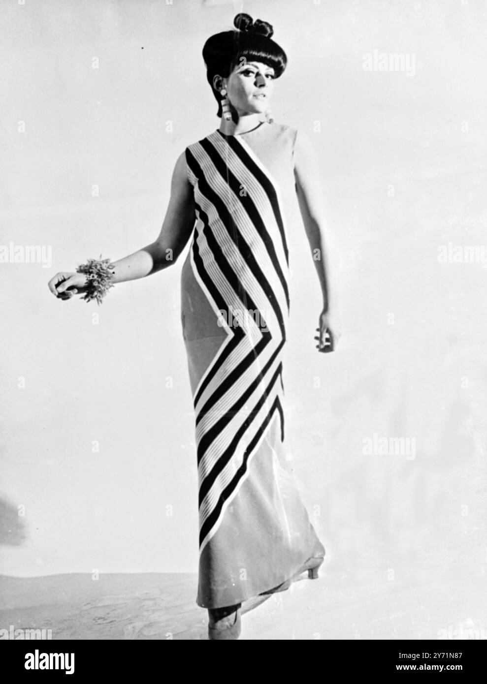Castillo Abendkleid Florenz, Italien: Auf dem Bild des Castillo of Rome Florence Fashion 1966 der Kollektion Frühling und Sommer zeigt sich dieses lange Abendkleid aus rot, orange, schwarz und gelb gestreifter Baumwolle. Das von OP-Art inspirierte Kleid hat einen Zick-Aging-Look, mit seinem diagonalen Design von der Schulter bis zum Saum. 18. Januar 1965 Stockfoto