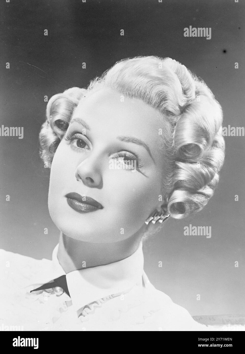 Edwardianisches Haar. Es gibt einen Rückblick auf edwardianische Styles in der neuesten Hair Do von Adele Jergens, Columbia Pictures Star. Das Haar ist auf der rechten Seite geteilt und die Oberseite in tiefe Wellen versetzt. Beide Seiten und der Rücken werden in gleichmäßigen Reihen von Locken platziert, die alle zum Gesicht gerichtet sind. Beim Auskämmen wird die obere Welle mit Nadeln in Position gehalten, das restliche Haar wird kräftig gebürstet und zu drei Locken auf beiden Seiten gerollt. August 1948 Stockfoto