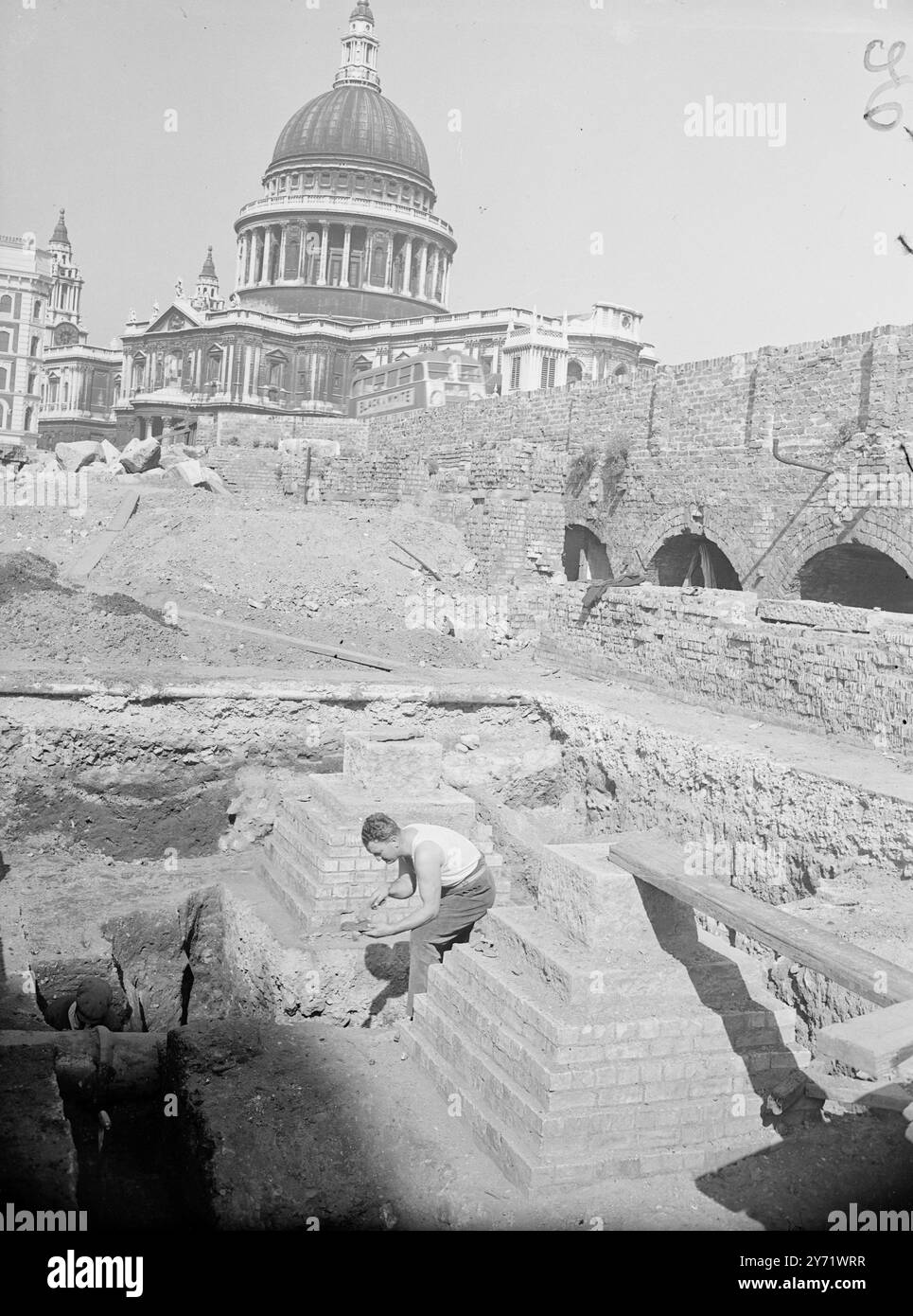 Suchen Sie nach einer Stadt. Inmitten der bombardierten Ruinen der City of London graben Männer in der Hoffnung, eine verlorene Stadt zu finden, die der Römer. Der Hauptstandort - einer von drei - befindet sich in der Cannon Street - Queen Victoria Street, östlich von St Paul's, dem Zentrum von Roman London. Bereits in der Nähe wurden Spuren römischer Bauten gefunden, aber die Arbeiten werden durch die modernen Fundamente und mittelalterliche Müllgruben behindert. Das Bild zeigt: Herr G R Faulkner, der sich freiwillig bei den Entführungen während des Urlaubs, der heute auf der Baustelle beschäftigt ist, unterstützt hat. St. Paul's Catherdral ist im Backgr zu sehen Stockfoto Suchen Sie nach einer Stadt. Inmitten der bombardierten Ruinen der City of London graben Männer in der Hoffnung, eine verlorene Stadt zu finden, die der Römer. Der Hauptstandort - einer von drei - befindet sich in der Cannon Street - Queen Victoria Street, östlich von St Paul's, dem Zentrum von Roman London. Bereits in der Nähe wurden Spuren römischer Bauten gefunden, aber die Arbeiten werden durch die modernen Fundamente und mittelalterliche Müllgruben behindert. Das Bild zeigt: Herr G R Faulkner, der sich freiwillig bei den Entführungen während des Urlaubs, der heute auf der Baustelle beschäftigt ist, unterstützt hat. St. Paul's Catherdral ist im Backgr zu sehen Stockfoto