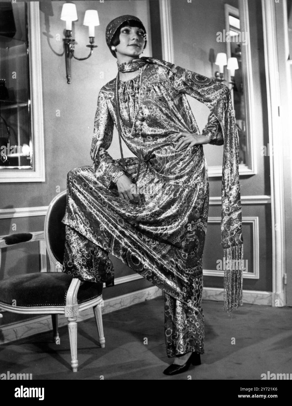 Dieses langärmelige Abendkleid , das über einer schlampigen Hose getragen wird , ist typisch für die Abendlinie , die Marc Bohan für das Haus Dior kreiert hat . Der lahme Gaze Stoff ist in einem brillanten persischen Teppich Farbschema. Ein langer, verführerischer Schal und ein eng anliegender Turban runden den orientalischen Look ab. Die Sandalen sind in dunkelblauem Lack mit klobigen Absätzen. Der Abendstil stammt aus Diors Herbst- und Winterkollektion 1969/70. 8. August 1969 Stockfoto
