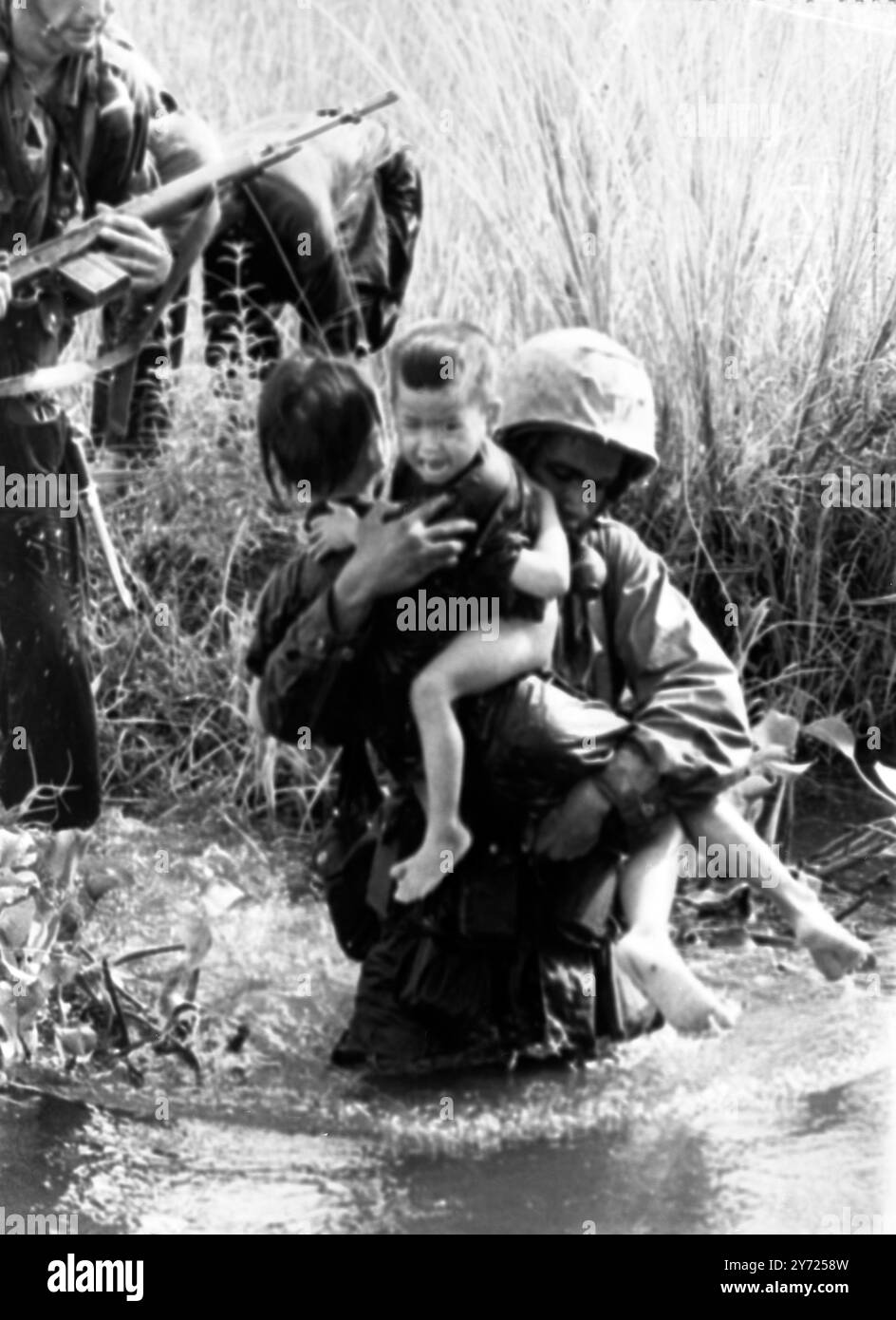 Der Vietnamkrieg Qui Nhon, Südvietnam; die Brutalität und Herzlosigkeit des Krieges wird deutlich in diesem Bild eines Soldaten dargestellt, der zwei weinende, verwaiste vietnamesische Kinder über einen Sumpf trägt. Es war ein typischer Vorfall, als amerikanische Truppen den verdeckten Viet Cong jagten. Später im Jahr sollte der Fotograf Kyoichi Sawada, aus Tokio, den World Photo Award mit einem weiteren Bild gewinnen, das er im selben Bezirk gemacht hat......... Eine Familie flüchtet vor einem Luftangriff auf ihr Dorf. 11. Dezember 1965 Stockfoto