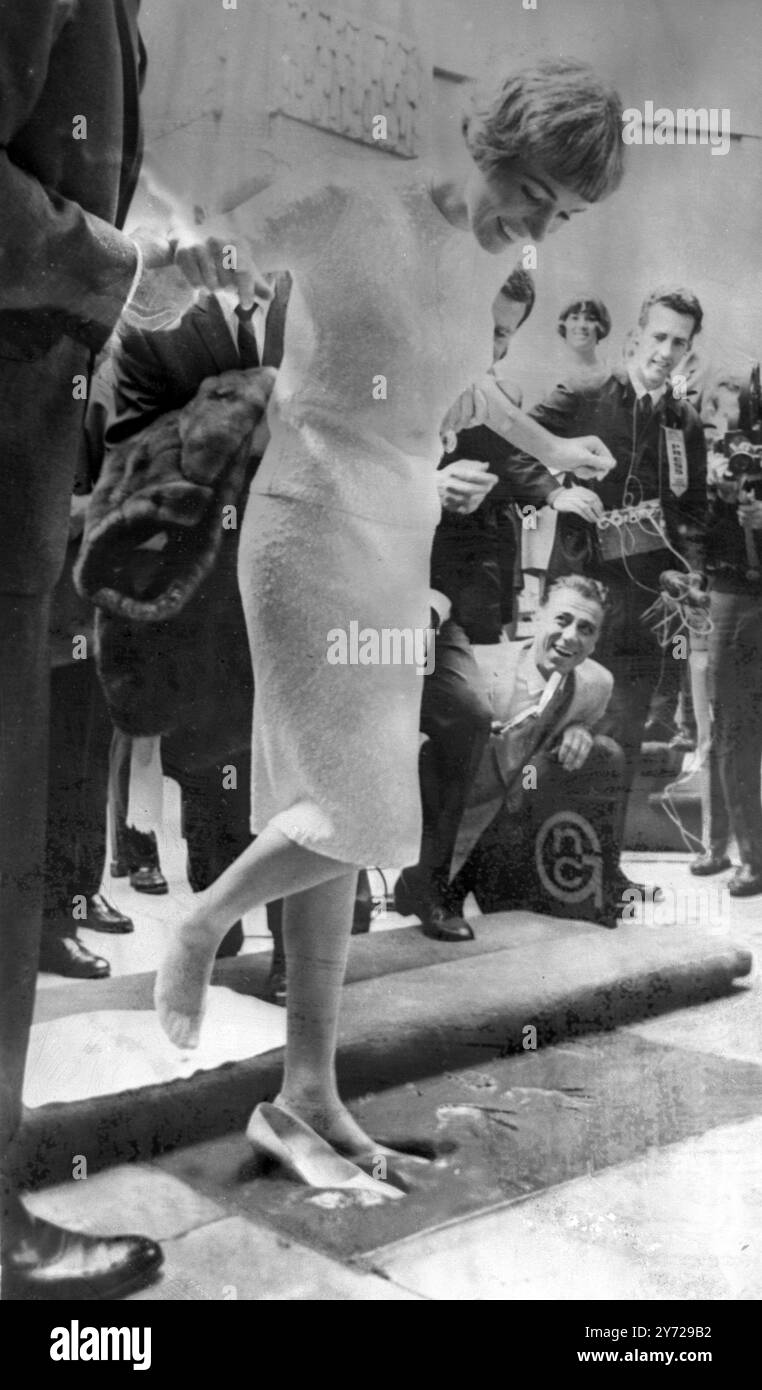 Die britische Schauspielerin Julie Andrews , die gestern in einer New Yorker Kritikerumfrage für ihre Rolle in The Sound of Music zur besten Schauspielerin des Jahres 1965 gewählt wurde , wirkt amüsant, als sie vor dem berühmten Grauman's Chinese Theatre in Hollywood aus ihren Schuhen herausgeholt wird , die in Zement stecken geblieben sind . 5. April 1966 Stockfoto