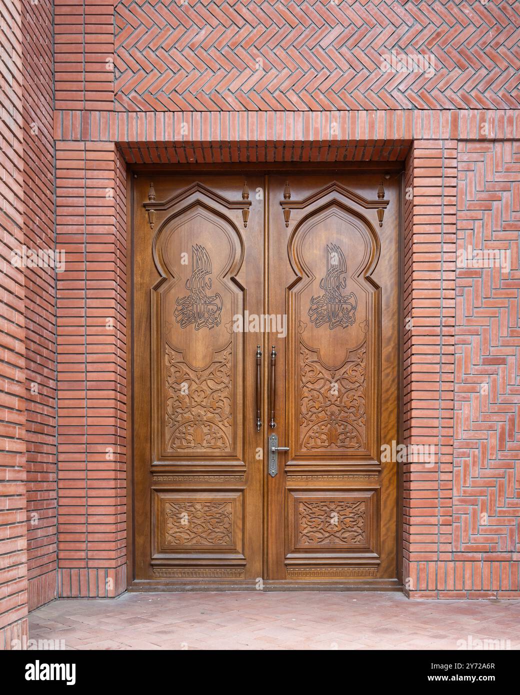 Kunstvolle Holztüren zeigen detaillierte Schnitzereien, die vor einem Hintergrund aus Ziegeln stehen und die Handwerkskunst und das Design hervorheben Stockfoto