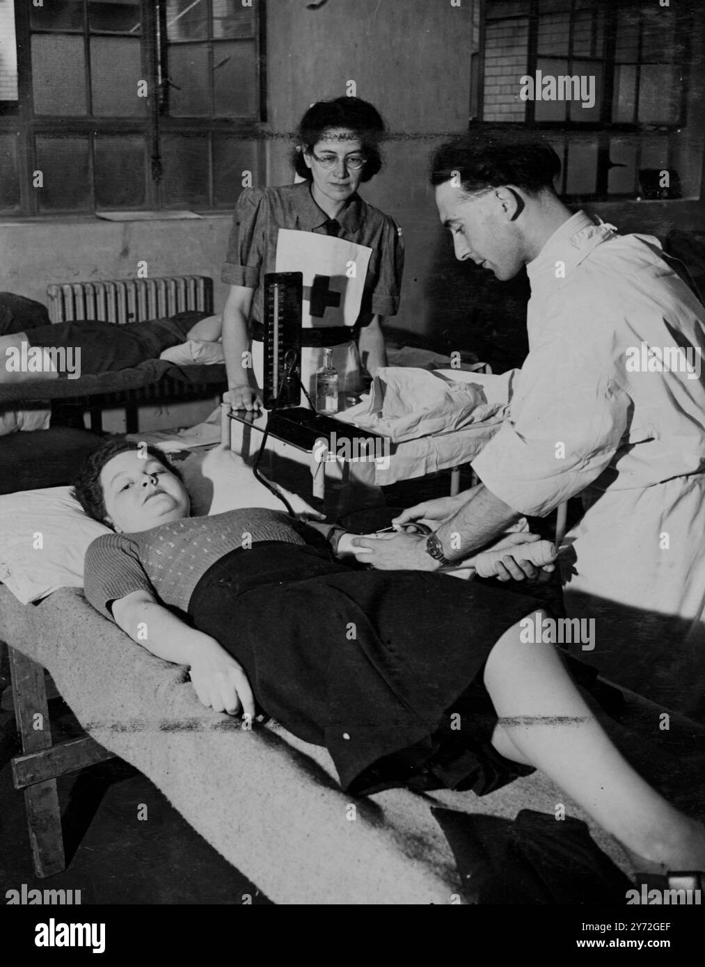 Miss Sheila Triggs, eine Betreiberin an der London Trunk Exchange und andere Mädchen von der London Trunk Exchange, Faraday Buildings, versammelten sich um die Antwort auf den Aufruf des Gesundheitsministers an alle Regierungsabteilungen für Spender des National Blood Transfusion Service. Hier nimmt Dr. Booth, stellvertretender Direktor des North London Blood Department, Blut von ihrem Arm in Faraday Buildings. 1. Juli 1947 Stockfoto