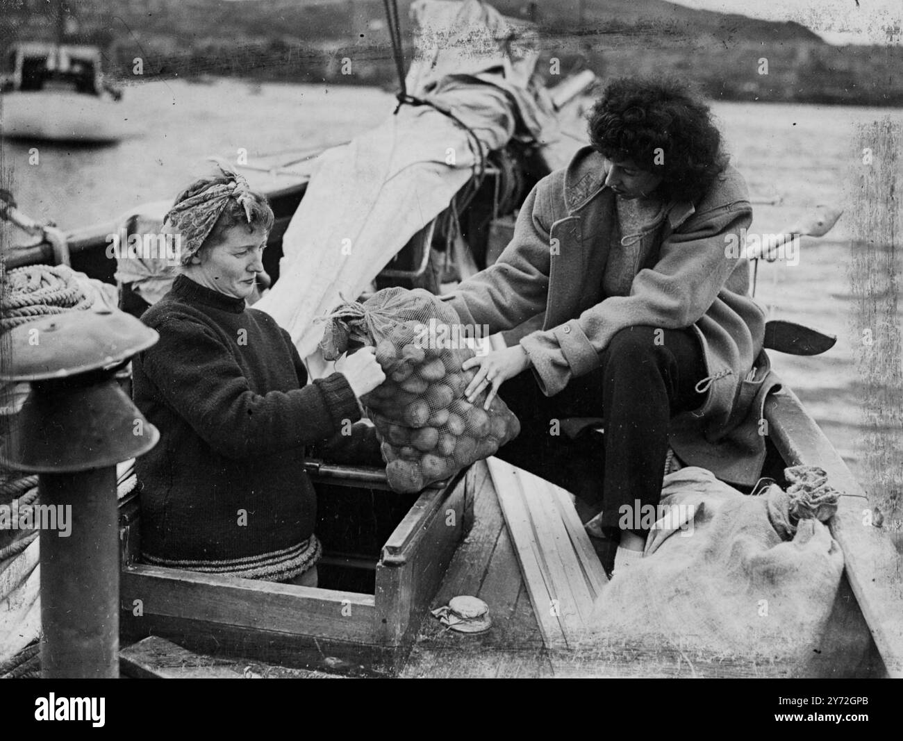 Fünf Leute brechen von Gourock auf, um die gefährliche 5500 Meilen lange Reise nach Amerika in 63 Fuß Yawl White Cloud zu versuchen. Neuer Kapitän des Schiffes ist der 22-jährige zweite Kamerad Roderick Finlayson aus Ross-shire, Schottland. Mit ihm geht es zu jungen Ex-Piloten der amerikanischen Luftwaffe und ihren Frauen. Gestern war die Party damit beschäftigt, die letzten Vorbereitungen für den langen Film zu treffen. Wenn alles gut läuft, hoffen sie, Anfang September in Maine anzukommen. Das Bild zeigt: Die Vorräte für die Reise werden an Bord der White Cloud in Gourock von den Ehefrauen der amerikanischen Ex-Piloten Mrs. Love (rechts) und genommen Stockfoto
