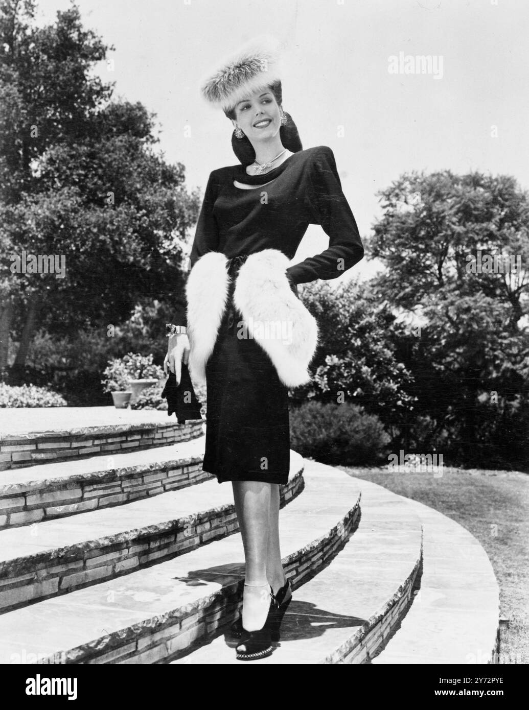 Columbia-Star Ann Miller betritt den Frühling in diesem eindrucksvollen Ensemble. Das Nachmittagskleid besteht aus schwarzer Wolle mit geschliffenem U-Ausschnitt, Dolman-Ärmeln und anmutig geschnittenen, geschwungenen Schulterklappen. Der Hut ist aus wunderschön gestaltetem Musquash und das Fell wiederholt sich als dekorative Hüftpolster auf dem Gehrock. Schwarze Wildlederschuhe mit offener Zehenpartie und attraktive goldene Ohrringe, Ketten und Armreif runden das schillernde Outfit ab, in dem ein strahlender Tag begrüßt wird. 19. Januar 1947 Stockfoto