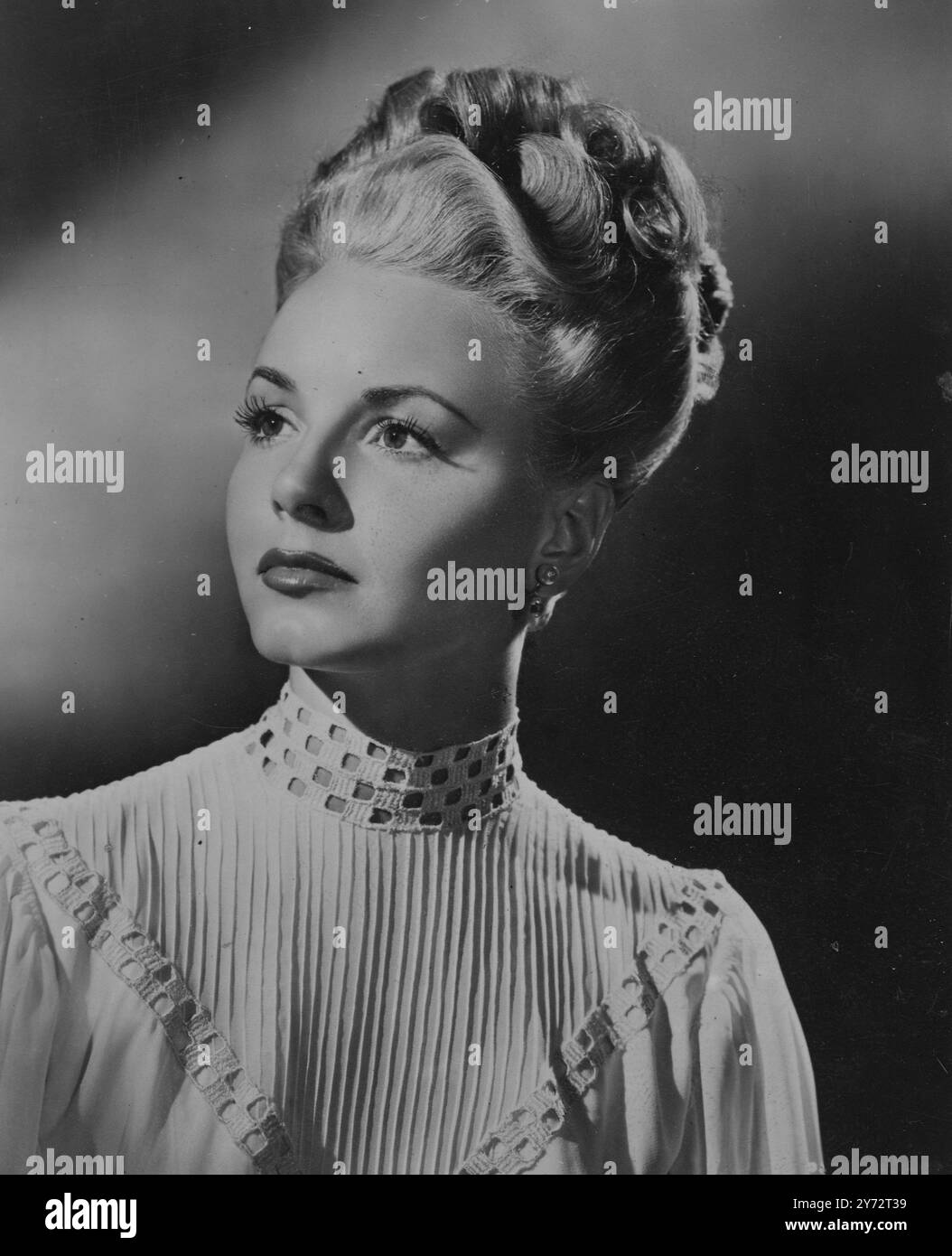 Columbia-Star Janet Blair trägt diese Frisur aus dem 19. Jahrhundert und einen Film „Gallant Journey“. Obwohl Janets Frisur so gestaltet ist, dass sie der Periode des Bildes entspricht, ist sie dank der einfachen Anordnung gut an die aktuellen Modi anpassbar. Das Haar wird sanft vom Gesicht weggeschwenkt und zu losen Locken gekämmt, die sich hoch auf dem Kopf stapeln. 7. Dezember 1946 Stockfoto