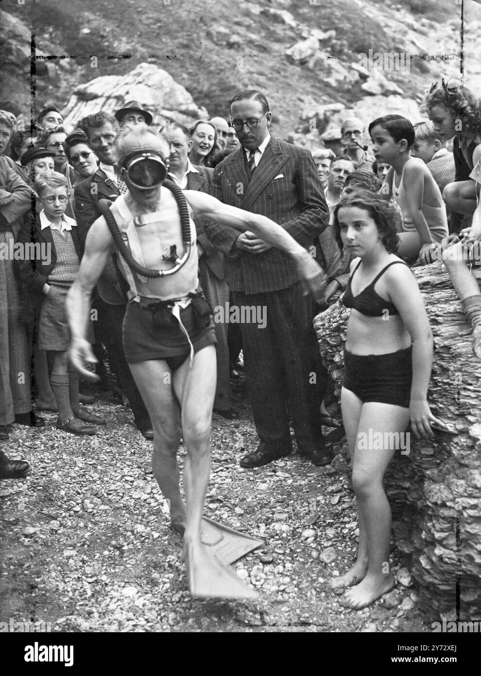Frogman neuer STYLE. Der 68-jährige, ehemalige Pariser Barrister Monsieur Daniel P Causteau Flaps ist weit hinunter zum Strand von Torquay, Devon, um zum ersten Mal in Großbritannien ein neues leichtes Tauchen-Outfit zu demonstrieren, die Erfindung seines Sohnes, Lt. Commander M. Jacques Yves Cousteau. Der Anzug, der aus nassen Füßen, einer großen Maske und einem Behälter mit Druckluft besteht, der auf dem Rücken umschnallt und mit einem Rohr am Mund befestigt ist, ermöglicht es dem Taucher, lange Zeit unter Wasser zu bleiben und dabei volle Bewegungsfreiheit zu haben. Bei der Torquay-Demonstration blieb Vater Cousteau für bescheidene neun Minuten unter, aber er ist erfunden Stockfoto