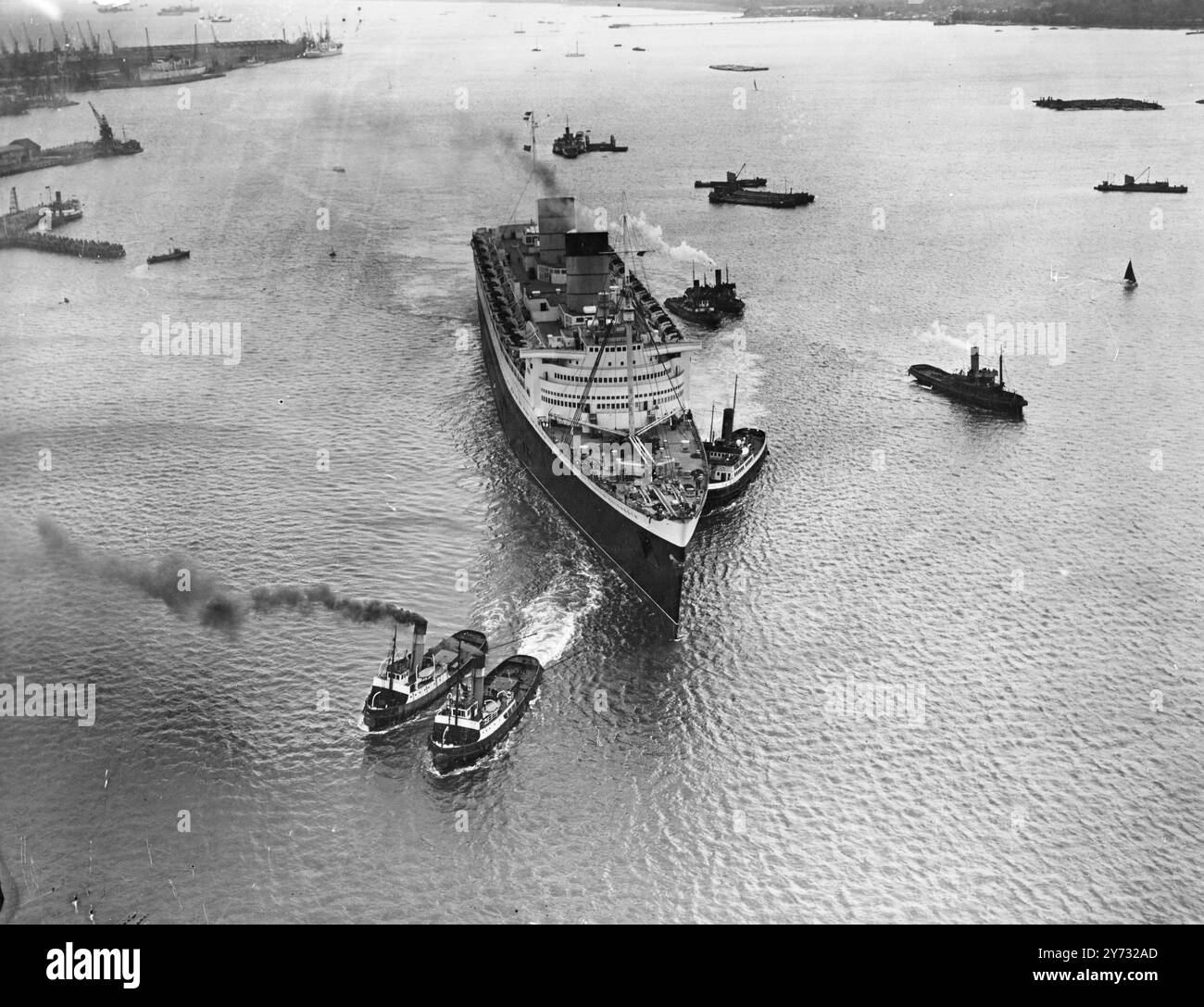 Die 83.000 Tonnen schwere Cunarder 'Queen Elizabeth', das größte Liner der Welt, kam heute von der Clyde nach Southampton, wo sie sich wieder als Luxusliner verkleidet hat. Das Bild zeigt: Eine beeindruckende Luftaufnahme der „Queen Elizabeth“, die neu mit schwarzem Loch, weißem Überbau und roten und schwarzen Trichtern bemalt wurde, während die Schlepper bei der Ankunft an den Docks von Southampton um sie herumschleppen. 16. Juni 1946 Stockfoto