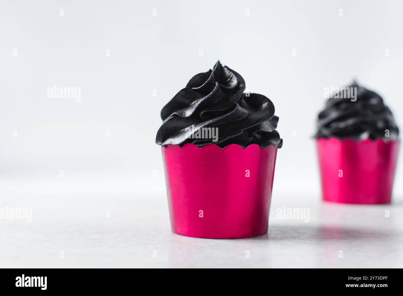 Pinke Cupcakes mit schwarzem Buttercremewirl, Cupcakes in rosa Folieneinlagen mit schwarzer Buttercreme, mattierte Halloween Valentinstag Cupcakes auf weißem Rücken Stockfoto