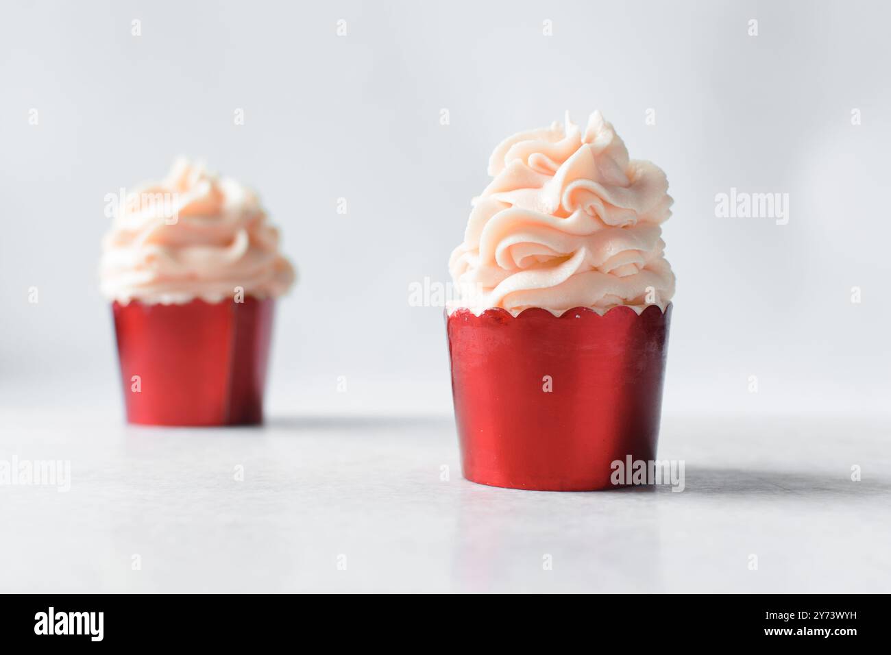 Rote Cupcakes mit rosafarbenem Buttercremewirl, Cupcakes in roter Folienfolie mit rosafarbener Buttercreme Stockfoto