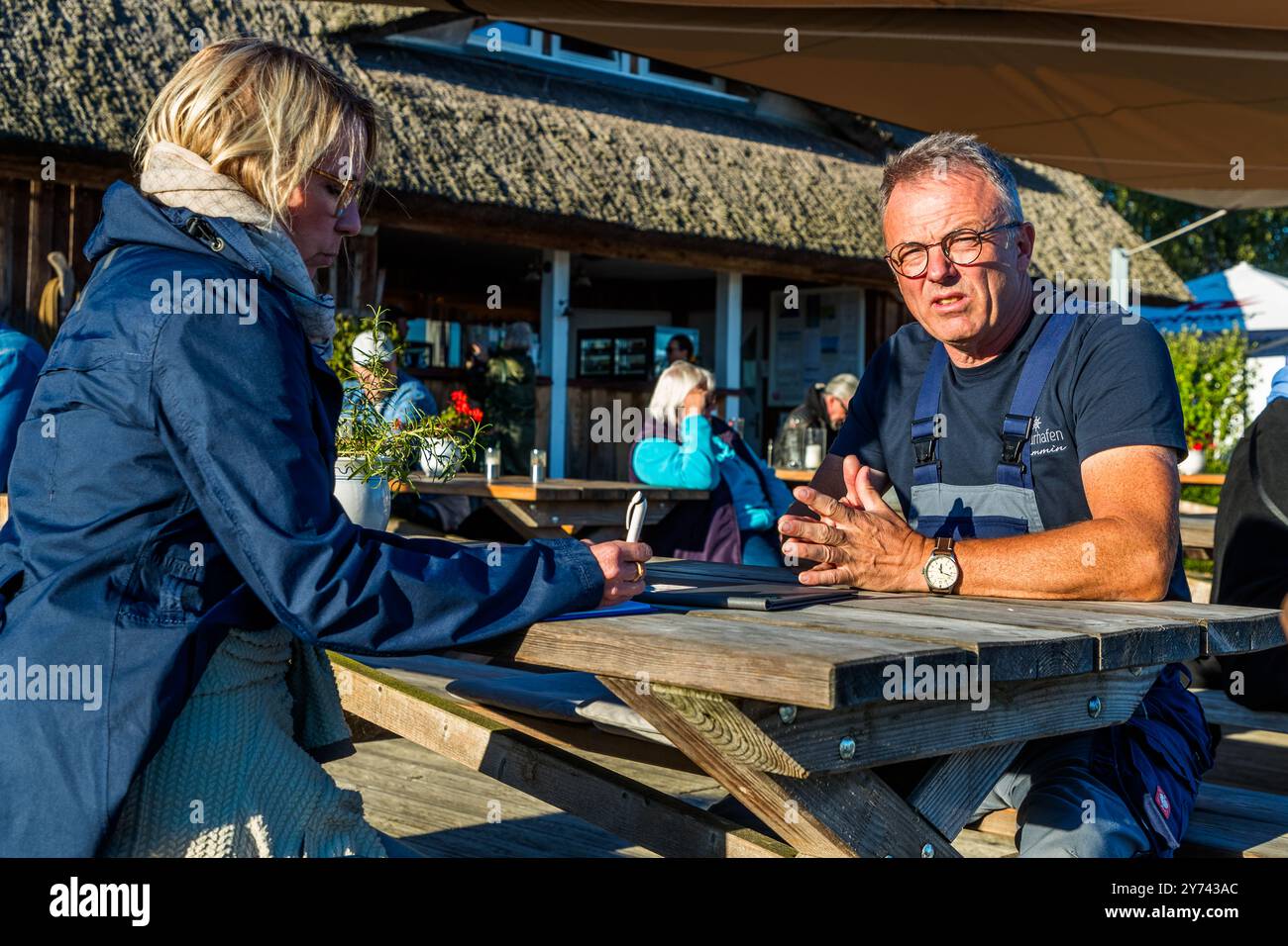 Journalistin Angela Berg spricht mit dem Hafenbesitzer Frank Schmidt am Steg des Naturhafens Krummin. Der eigentümergeführte Privathafen auf Usedom verfügt über eine Marina, Hausboote und Restaurants. Dorfstraße, Am Peenestrom, Mecklenburg-Vorpommern, Deutschland. Stockfoto