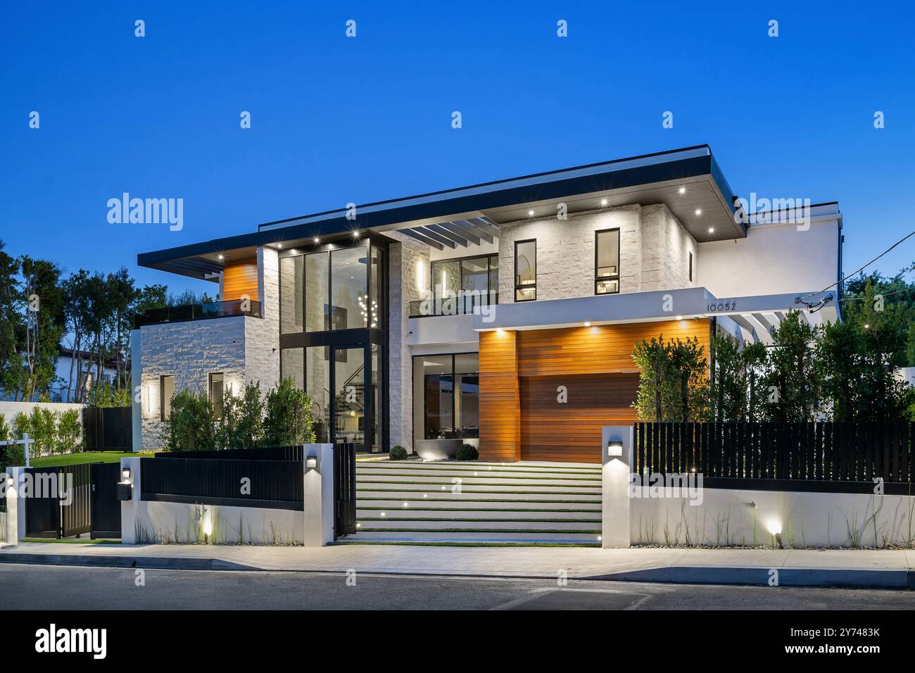 Modernes Luxushaus mit großen Fenstern, Gartenanlage und Abendbeleuchtung. Stockfoto