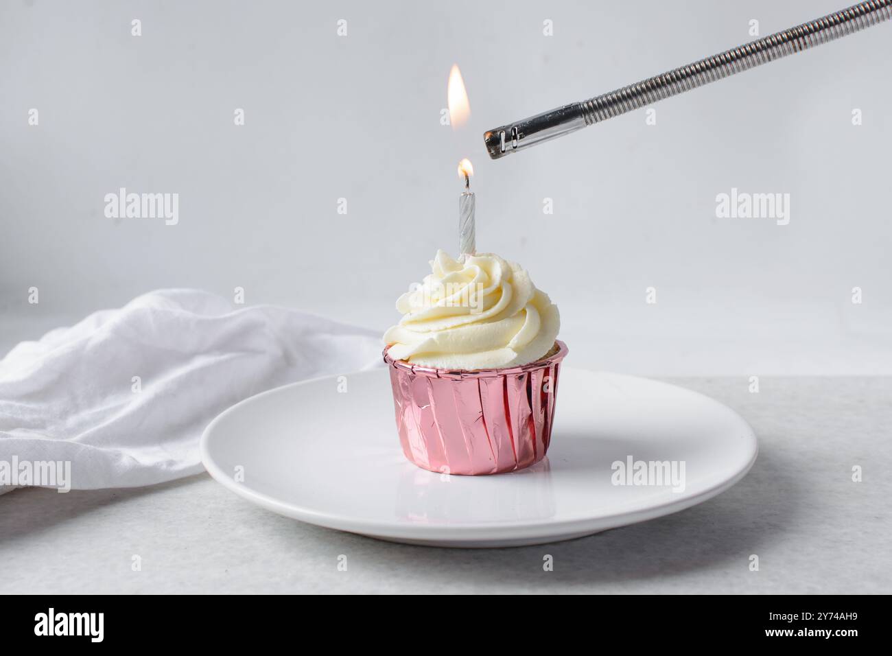 Rosafarbene Cupcakes mit hohem Buttercremewirbel und einer beleuchteten Kerze, Cupcakes in rosafarbenen Folieneinlagen mit Vanille-Buttercreme und einer Kerze Stockfoto