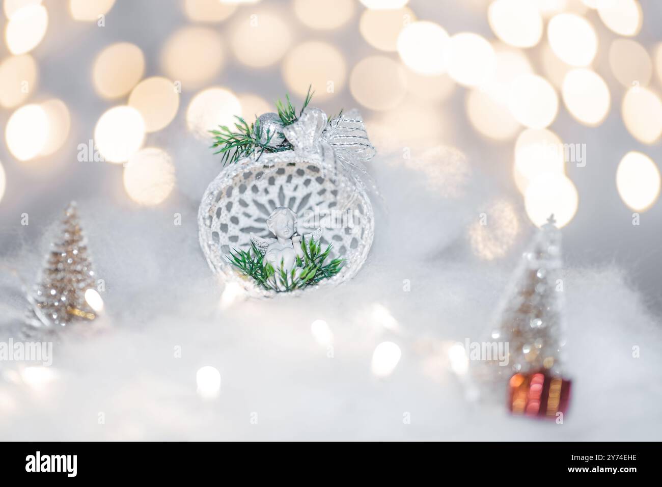 Weihnachtsdeo-Konzept an Feiertagen mit einem Porzellanengel, weißem Kunstschnee für einen festlichen dezember. Im Hintergrund befinden sich Bokeh-Kugeln aus LIGH Stockfoto