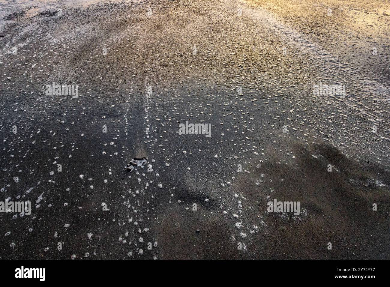 Wellen an einem Sandstrand, die wunderschöne farbige Muster im Glanz des Sonnenuntergangs bilden. Stockfoto