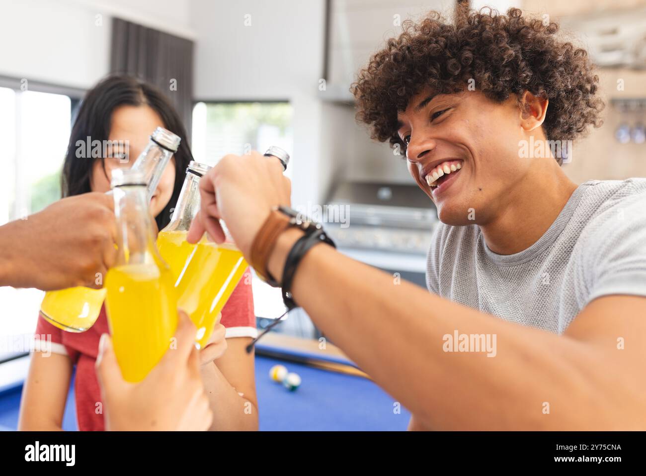 Verschiedene Freunde, die mit Flaschen Limonade toasten und die gemeinsame Zeit drinnen oder zu Hause genießen Stockfoto