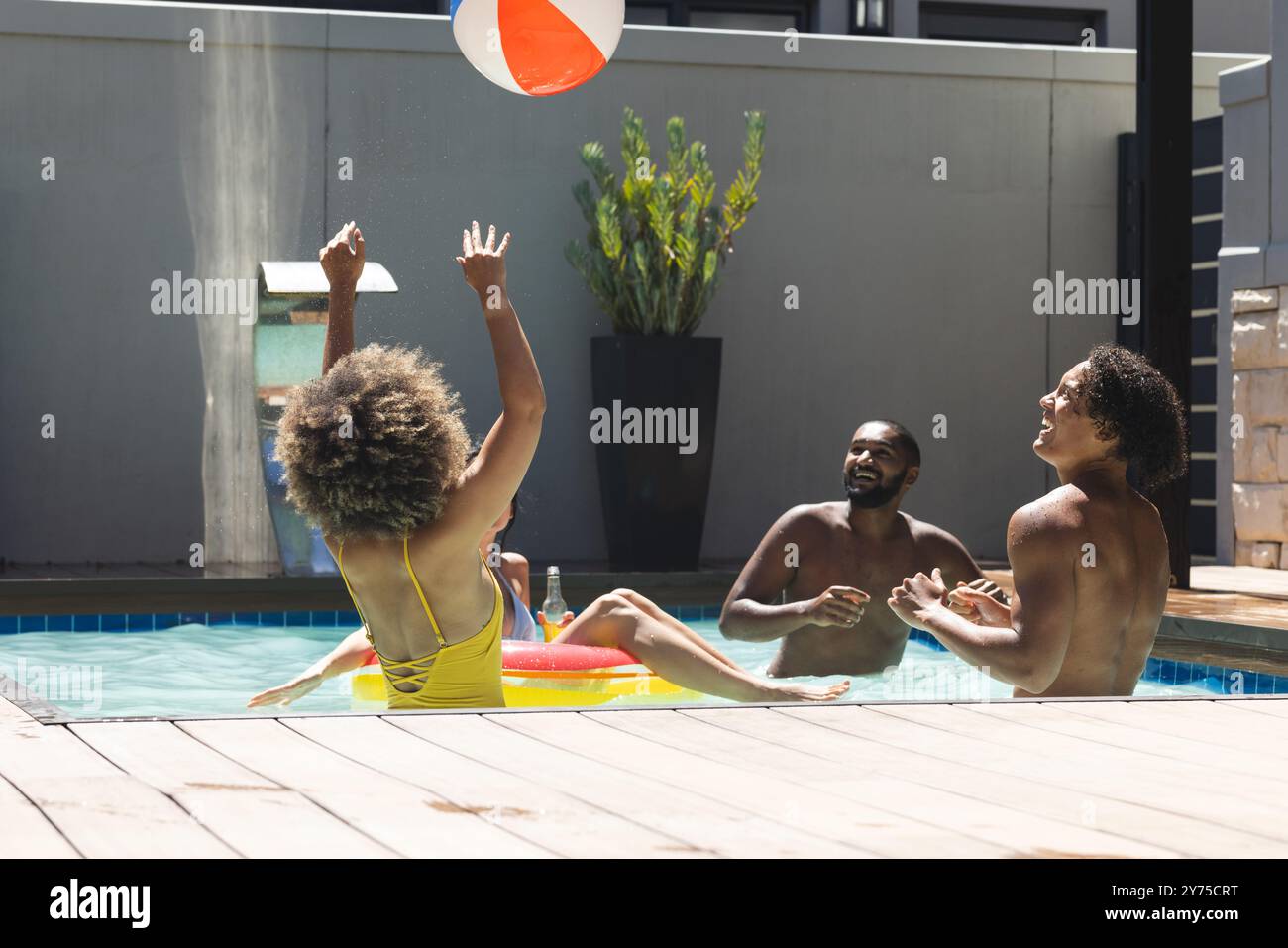Spielen mit Beachball, verschiedene Freunde genießen Poolparty an sonnigen Tagen, zu Hause Stockfoto