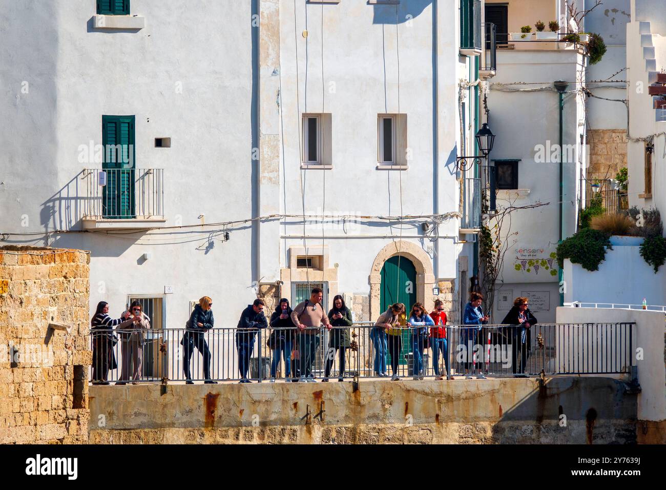 Eine Gruppe von Personen genießt die Aussicht von einer Terrasse in der Via Porto, der Altstadt von Polignano a Mare, Italien. Stockfoto