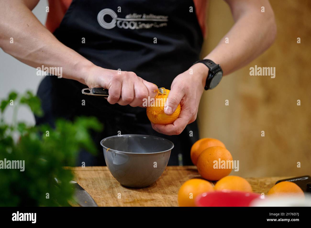 Nahaufnahme eines Mannes, der beim Kochen von Clas eine Orange über einer schwarzen Schüssel mit anderen Orangen im Hintergrund schält Stockfoto