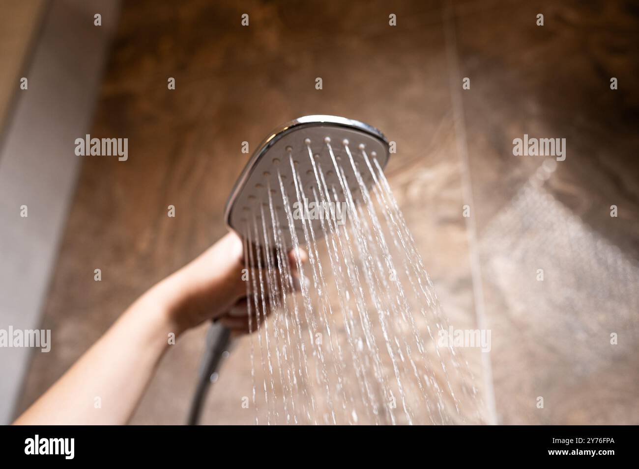 Die Hand einer Frau hält beim Duschen einen Duschkopf. Nahaufnahme der Hand und des Wasserstroms Stockfoto
