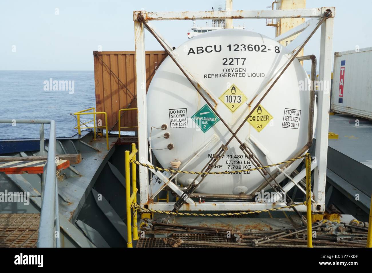 Weißer Container, der mit Stangen und Drehschlössern an Deck des Containerschiffs verzurrt ist, mit Aufklebern für Gefahrgut. Stockfoto