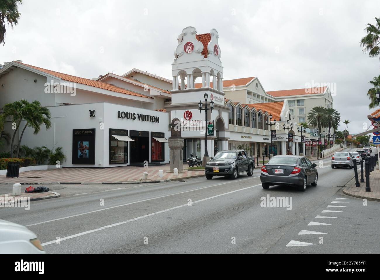 Hauptstraße mit modernen Gebäuden mit Luxusgeschäften, Palmen und neuen Autos in Oranjestad auf Aruba während des Frühlings unter bedecktem Himmel. Stockfoto