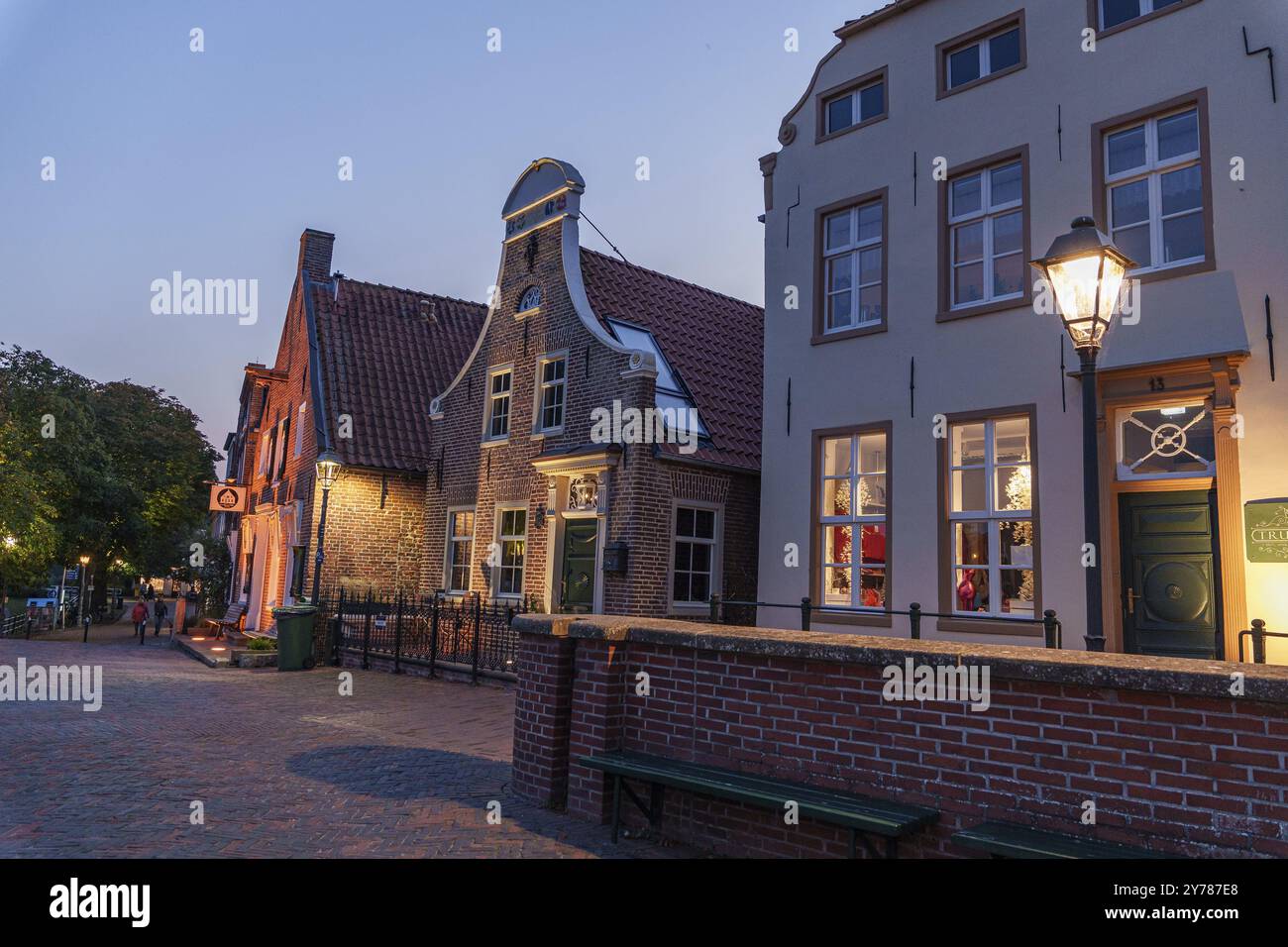 Historische Häuser und beleuchtete Schaufensterfenster in einer Straße in der Abenddämmerung, Greetsiel, Ostfriesland, Deutschland, Europa Stockfoto