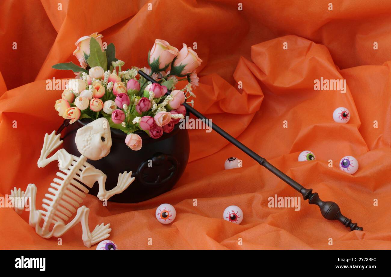 Gruseliges Totenfroschskelett, Plastikaugenkugeln, Zauberstab und schwarzer Hexenkessel als Blumenvase auf einem Halloween-Tisch. Stockfoto