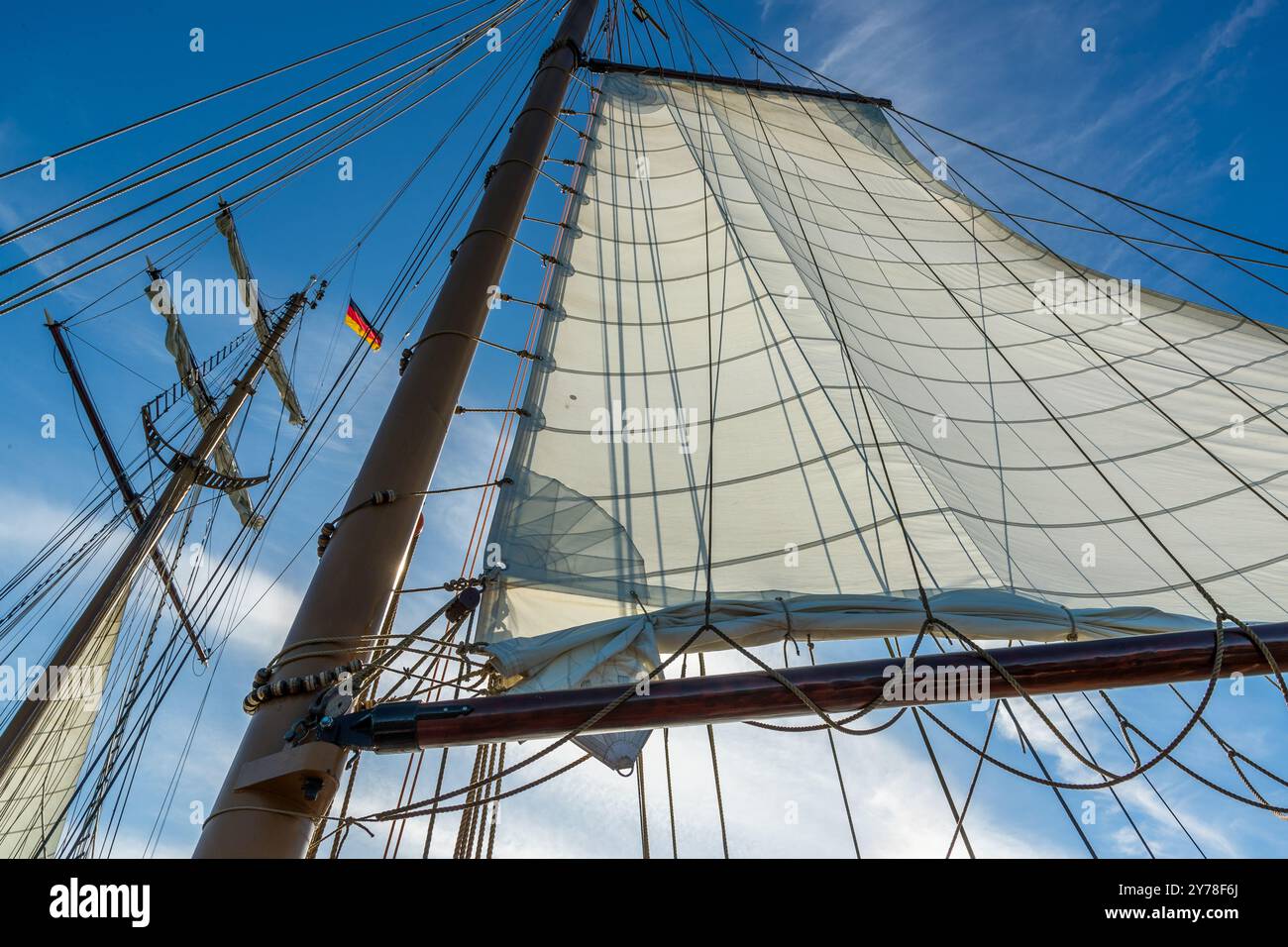 Das Großsegel der Weisse Düne bauscht sich weiß vor einem tiefblauen Himmel, die deutsche Flagge weht von der Takelage dahinter. Der Topsail-Schooner trägt diesen Namen seit 1964, nach dem weißen Dünenstrand auf der Nordseeinsel Norderney, zu dem er einst als Frachtschiff Baumaterialien transportierte. Achterwasser vor Usedom, Mecklenburg-Vorpommern, Deutschland. Stockfoto
