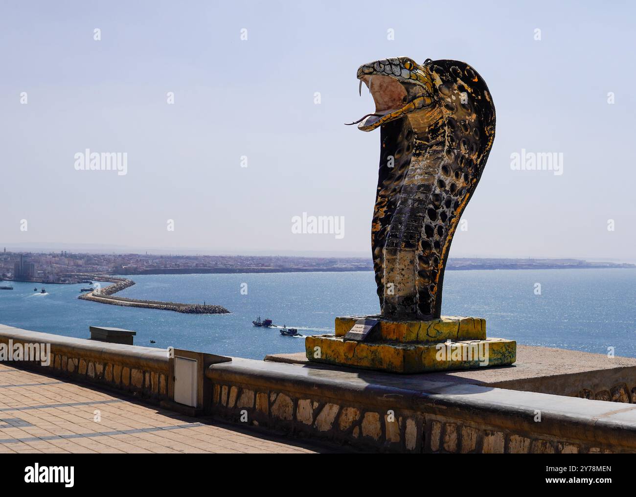 Große Aussicht und eine Landschaft mit der 'Schlangenstatue' am Place of Rass lafaa in Safi Marokko mit einem großen blauen Meer mit Fischerbooten und der Stadt Stockfoto