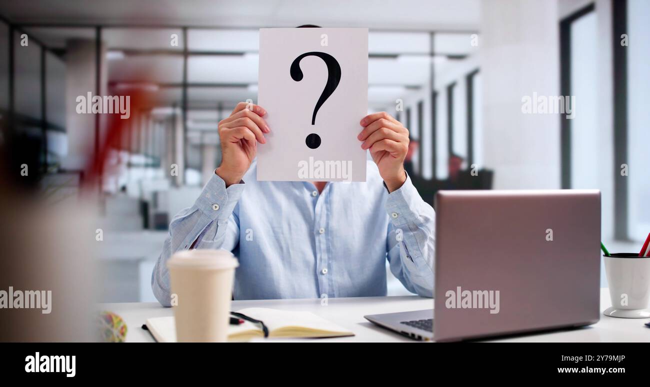 Geschäftsmann Mit Fragezeichen Vor Dem Gesicht Am Schreibtisch Im Büro Stockfoto