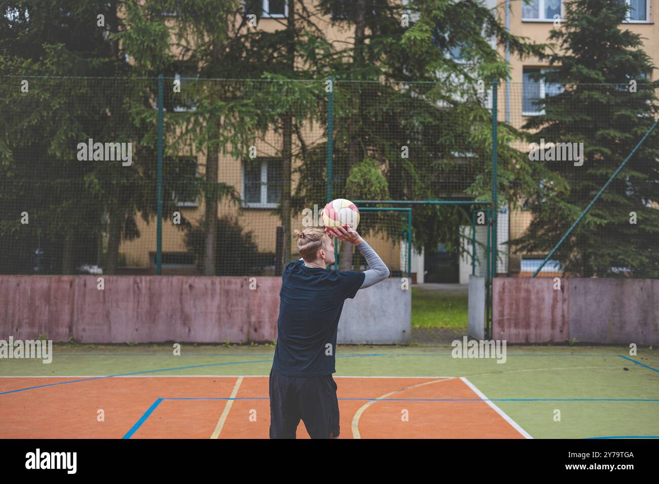 Der Basketballspieler bereitet sich darauf vor, den Ball auf einem Platz im Freien zu schießen und positioniert sich für einen konzentrierten Wurf. Die Szene fängt den Athleten in der Mitte der Bewegung ein, Stockfoto