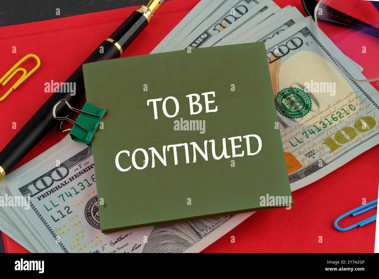 DER Text WIRD auf einem grünen Aufkleber auf dem Hintergrund von Dollarscheine auf dem roten Buch geschrieben Stockfoto
