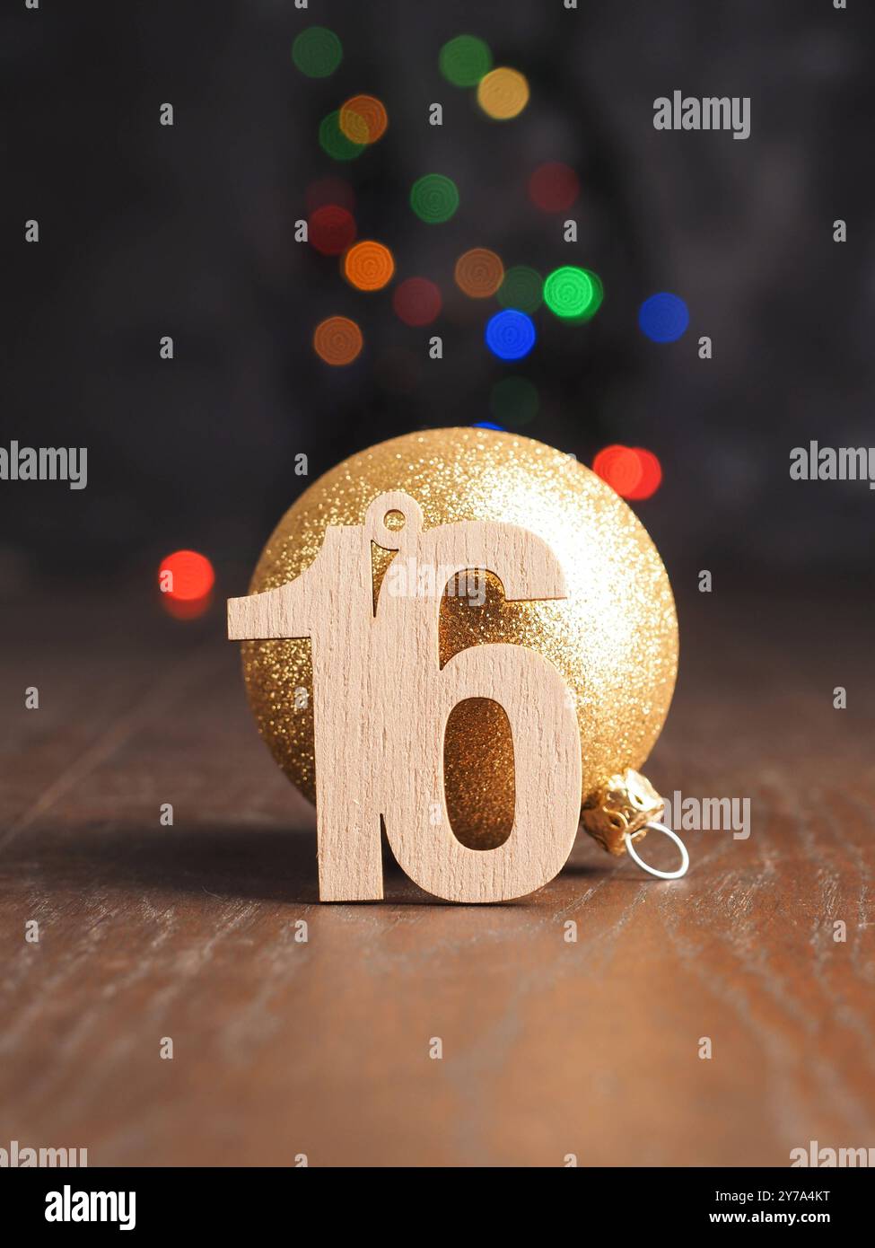 16. Dezember, hölzerne Nummer 16 mit einer goldenen Weihnachtskugel auf verschwommenen Weihnachtslichtern Stockfoto