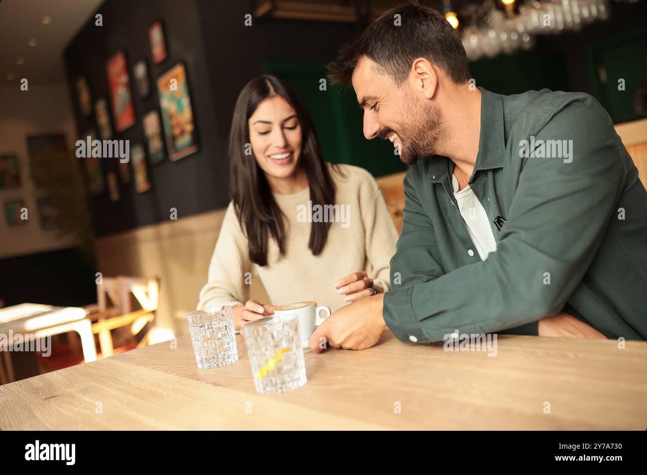 Zwei Freunde teilen sich Lachen und warme Drinks in einem charmanten Café und schaffen eine einladende Atmosphäre, die an einem sonnigen Tag die Verbindung und Freude feiert Stockfoto