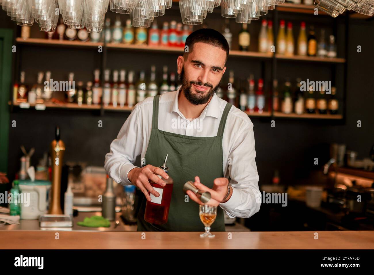 In einer lebhaften Bar mischt ein selbstbewusster Barkeeper einen frischen Cocktail und zeigt sein Know-how mit einer Flasche in der Hand, bereit für die Hektik der Nacht Stockfoto