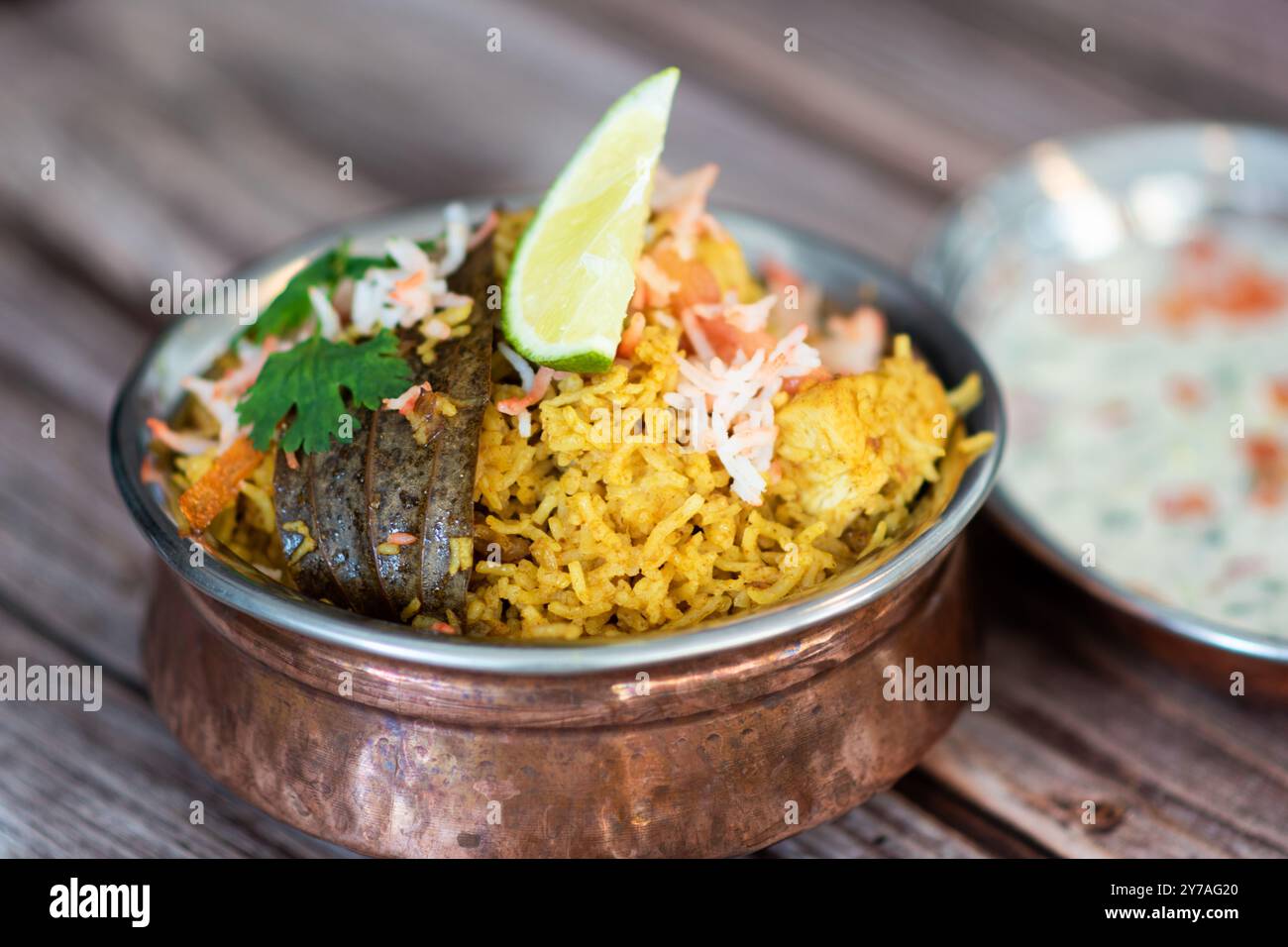 Würziger indischer Biryani-Pulao in goldener Schüssel mit indischem Basmati-Reisgericht mit Hühnerfleisch-Curry Ramadan Kareem, Eid. Servierschale aus Messing mit weißem Rücken Stockfoto