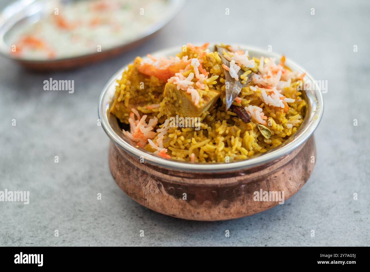 Würziger indischer Biryani-Pulao in goldener Schüssel mit indischem Basmati-Reisgericht mit Hühnerfleisch-Curry Ramadan Kareem, Eid. Servierschale aus Messing mit weißem Rücken Stockfoto