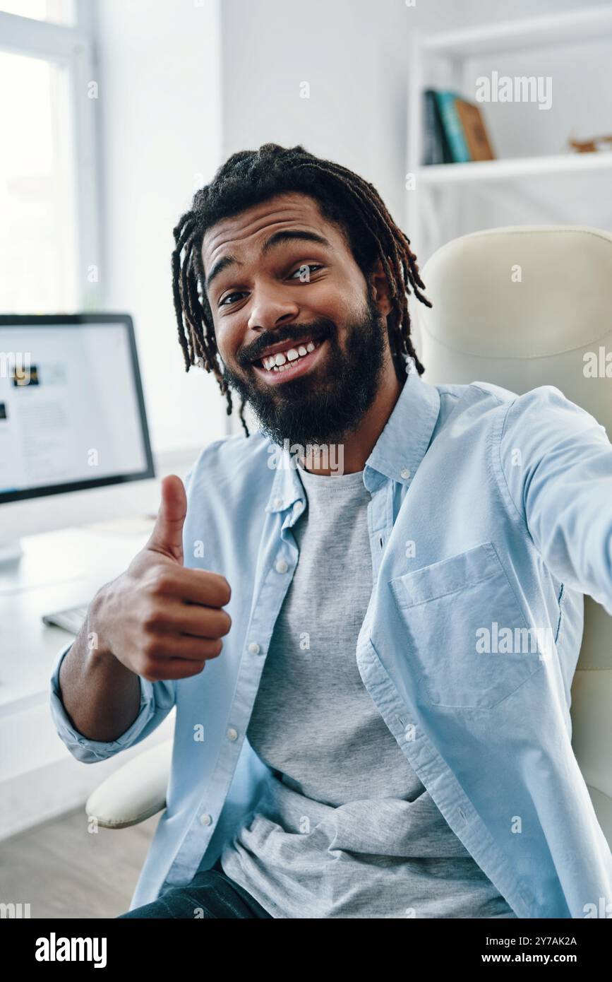 Ein verspielter junger afrikanischer Mann, der lächelt und in die Kamera schaut, während er drinnen Selfie macht Stockfoto