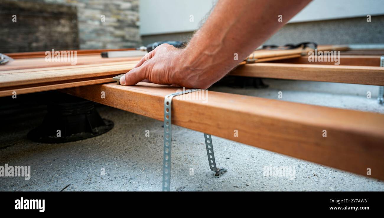 Flacher Blick auf die männliche Hand, die einen Kunststoff-Distanz zwischen Holzdielen platziert, während er eine neue renovierte Außenterrasse auf einer Grundkonstruktion baut Stockfoto
