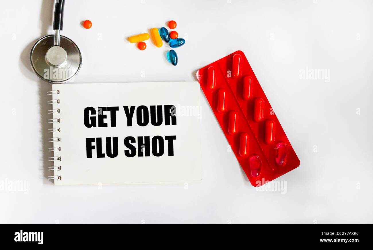 Erhalten Sie Grippe-Shot-Text auf Papierkarte mit Stethoskop und Pillen Top View auf weißem Hintergrund Stockfoto