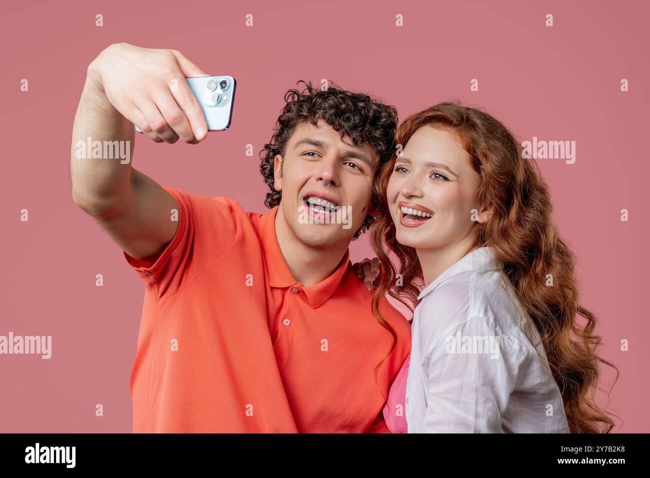 Glückliche Paare sprechen Kamera als Videoanruf, chatten, Selfie machen oder Vlog aufnehmen als Blogger auf rosa Studiowand Hintergrund. Hohe Qualität Stockfoto