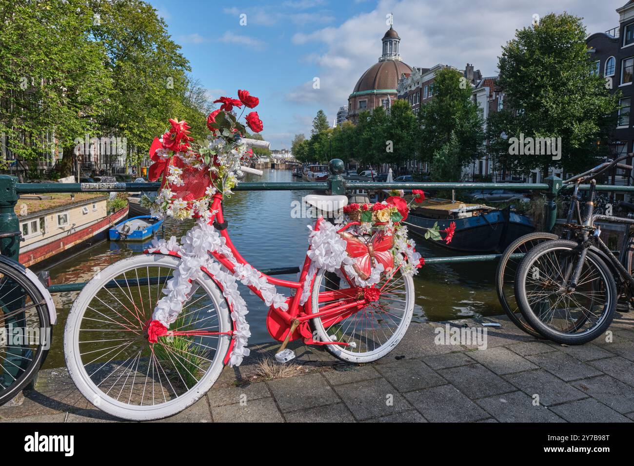 Farbenfrohes Fahrrad mit Blumen auf einer Brücke über den Singelkanal, Old Round Lutherische Kirche im Hintergrund, in Amsterdam, Niederlande Stockfoto