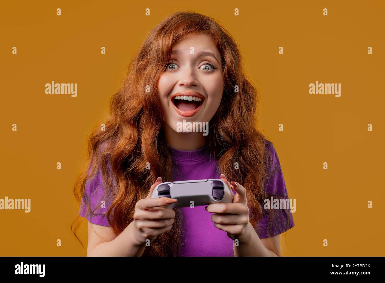 Hübsche junge Frau, die ein aufregendes Videospiel im Fernsehen spielt, mit Gamepad isoliert auf gelbem Studiohintergrund. Mit moderner Technologie. E-Sport, Hobby, Strea Stockfoto